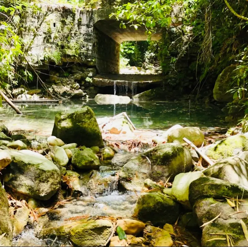 River pool over mossy boulders below a small stone bridge and waterfall